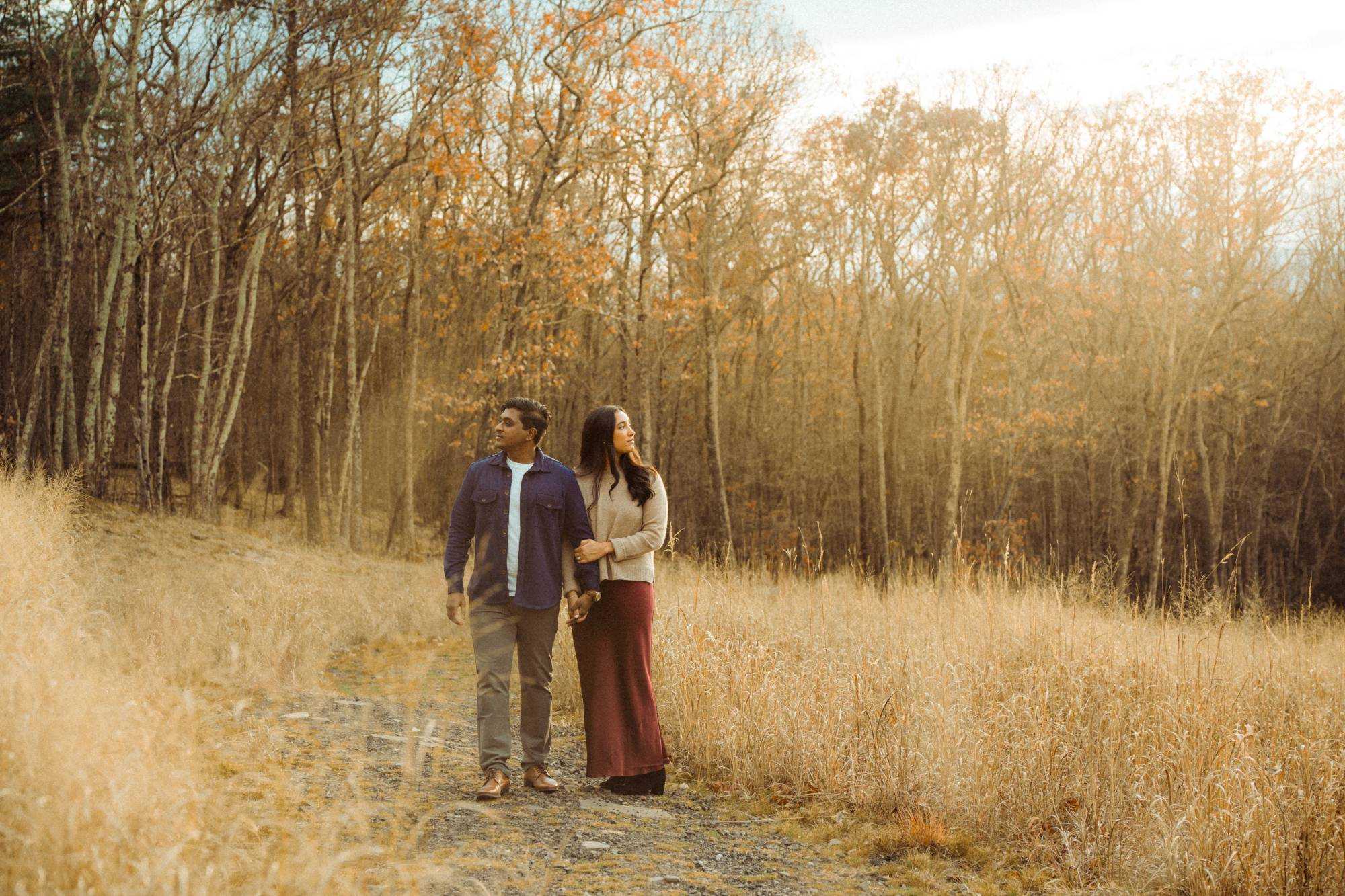 Myra and Rakesh walking arm in arm along a path through a golden autumn field